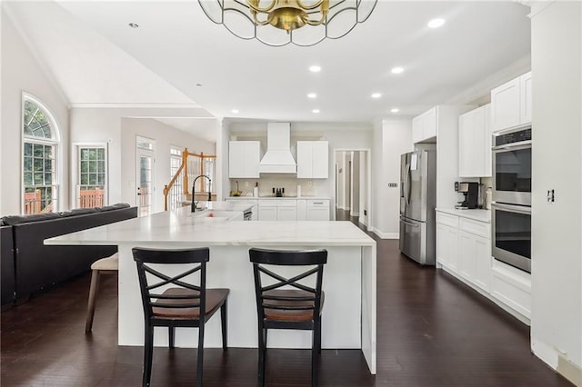 kitchen with stainless steel appliances, light stone counters, custom range hood, white cabinets, and a kitchen bar