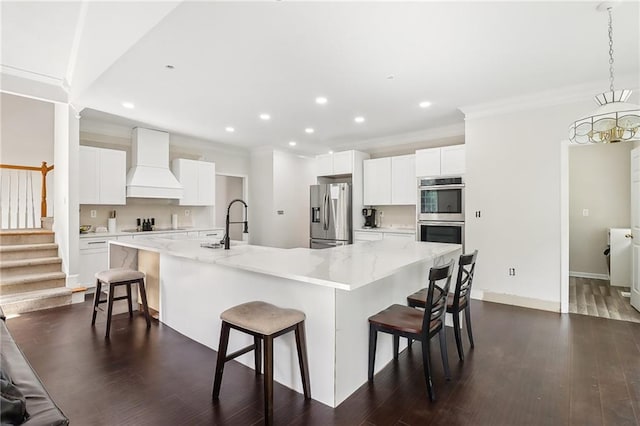 kitchen with appliances with stainless steel finishes, a breakfast bar area, white cabinets, custom exhaust hood, and a large island with sink