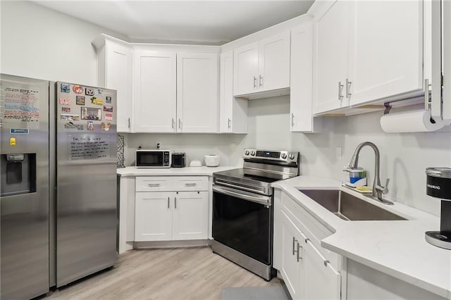 kitchen featuring sink, white cabinetry, appliances with stainless steel finishes, light stone countertops, and light hardwood / wood-style floors