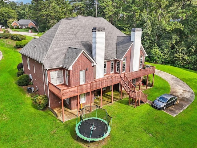 rear view of property with a deck, a yard, and a trampoline