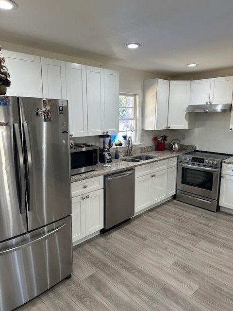kitchen with light wood finished floors, appliances with stainless steel finishes, under cabinet range hood, white cabinetry, and a sink