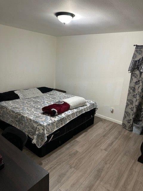 bedroom featuring light wood-style flooring, baseboards, and a textured ceiling