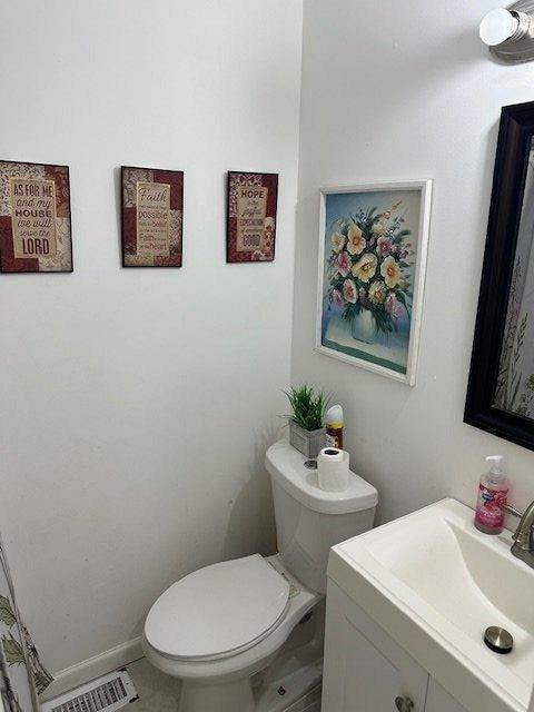 half bath with toilet, vanity, visible vents, and baseboards