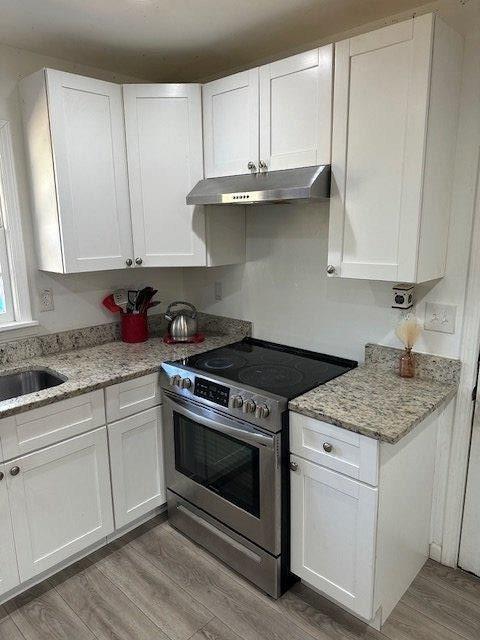 kitchen with electric stove, light stone counters, light wood-type flooring, under cabinet range hood, and white cabinetry