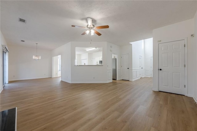 unfurnished living room featuring ceiling fan with notable chandelier, a textured ceiling, and light hardwood / wood-style floors