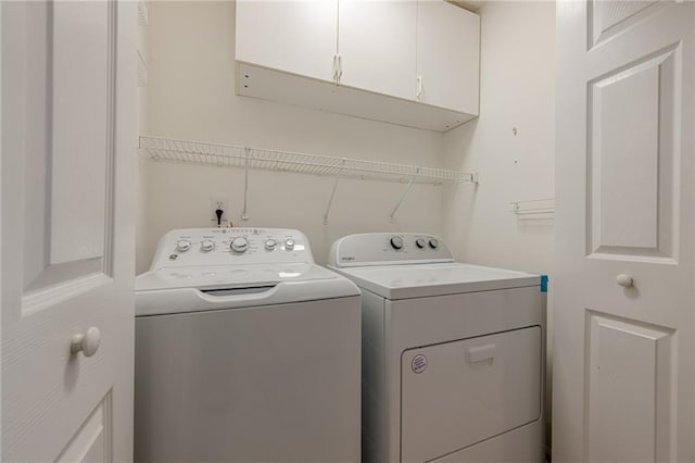 clothes washing area with washer and clothes dryer and cabinets