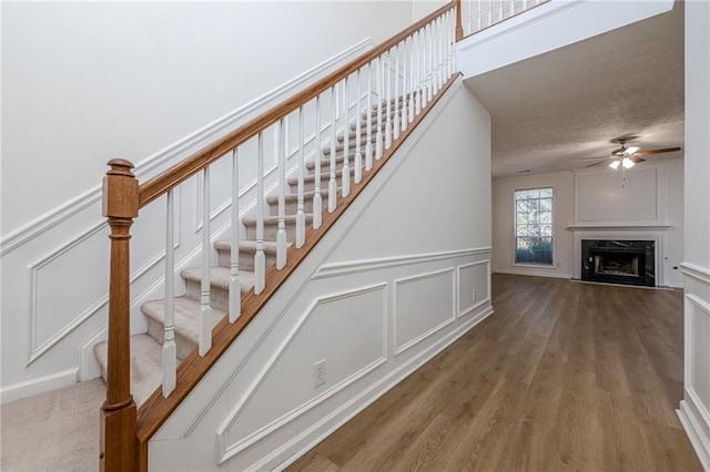 stairway featuring wood-type flooring, a fireplace, and ceiling fan