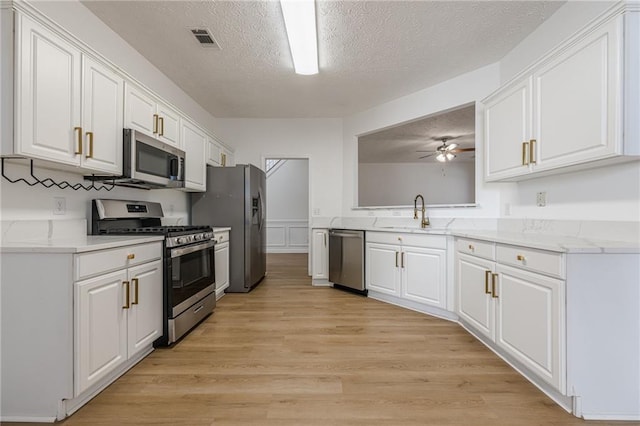 kitchen with sink, stainless steel appliances, a textured ceiling, white cabinets, and light wood-type flooring