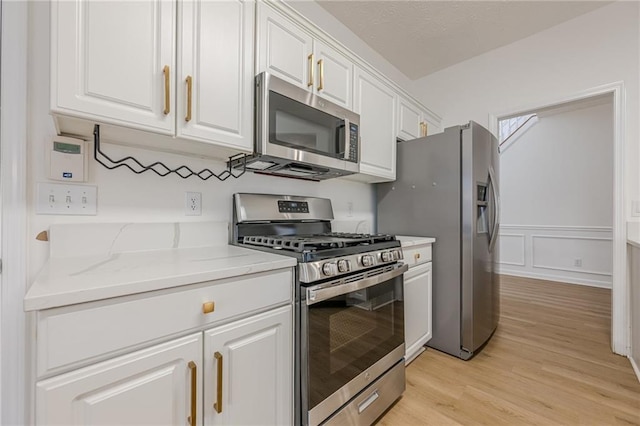 kitchen featuring white cabinetry, stainless steel appliances, light stone countertops, and light wood-type flooring