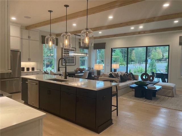 kitchen with freestanding refrigerator, white cabinetry, a center island with sink, and a sink