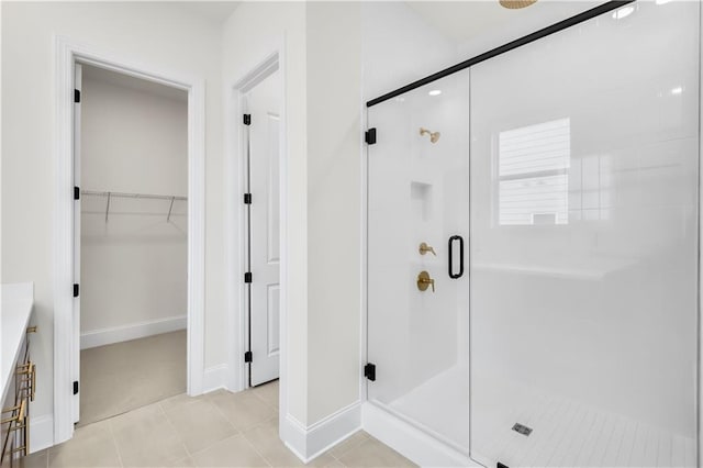 full bath featuring baseboards, a spacious closet, a stall shower, and tile patterned floors