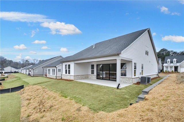 rear view of property featuring cooling unit, a shingled roof, a yard, a residential view, and a patio area