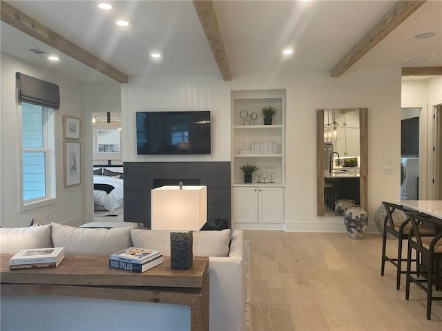 living room with built in shelves, light hardwood / wood-style flooring, and beamed ceiling