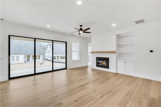 unfurnished living room featuring built in features, a glass covered fireplace, light wood-type flooring, and baseboards