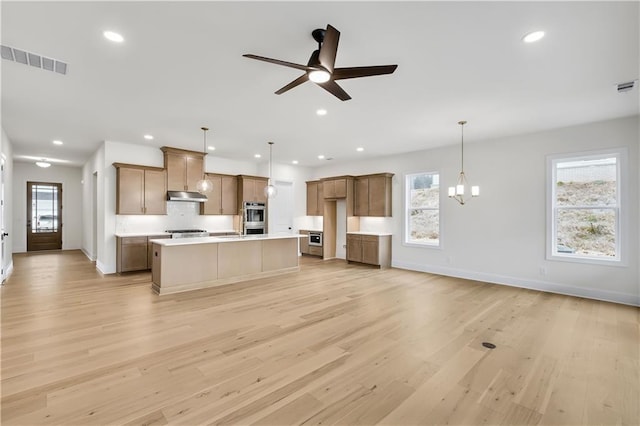 kitchen with hanging light fixtures, an island with sink, light countertops, and visible vents