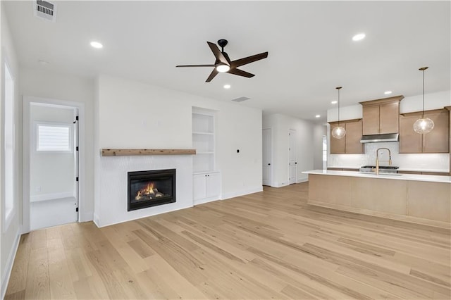 kitchen featuring under cabinet range hood, visible vents, open floor plan, hanging light fixtures, and light countertops