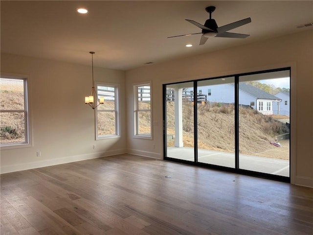 empty room with dark hardwood / wood-style flooring, ceiling fan with notable chandelier, and a wealth of natural light