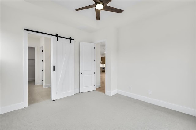 unfurnished bedroom featuring light carpet, a barn door, baseboards, ceiling fan, and a spacious closet