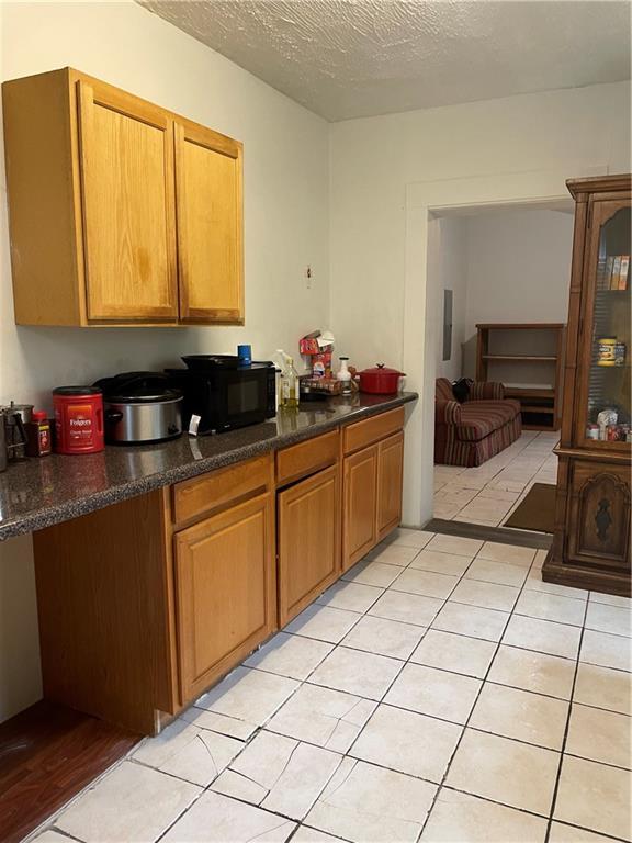 304 E 19th St SW, Rome, GA 30161 - kitchen featuring black microwave, dark countertops, a textured ceiling, light tile patterned floors, and brown cabinetry
