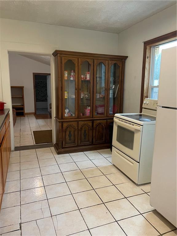 304 E 19th St SW, Rome, GA 30161 - kitchen featuring white appliances, light tile patterned floors, glass insert cabinets, a textured ceiling, and dark countertops