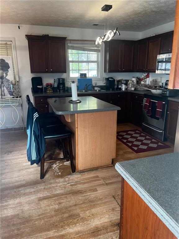 kitchen with stainless steel appliances, decorative light fixtures, a breakfast bar, light hardwood / wood-style floors, and a center island