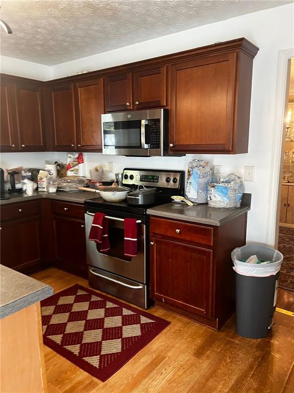 kitchen with a textured ceiling, light hardwood / wood-style floors, and stainless steel appliances