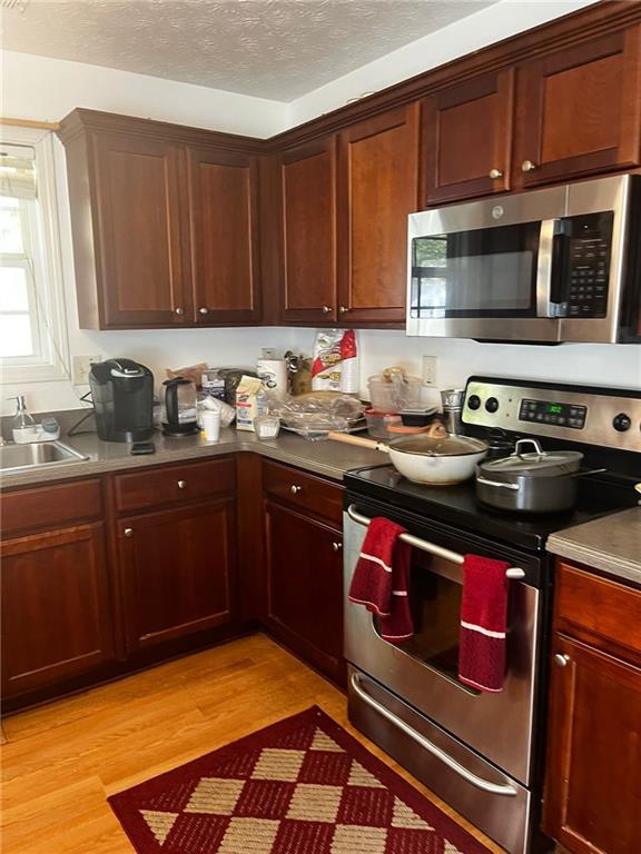 kitchen featuring a textured ceiling, sink, light wood-type flooring, and appliances with stainless steel finishes