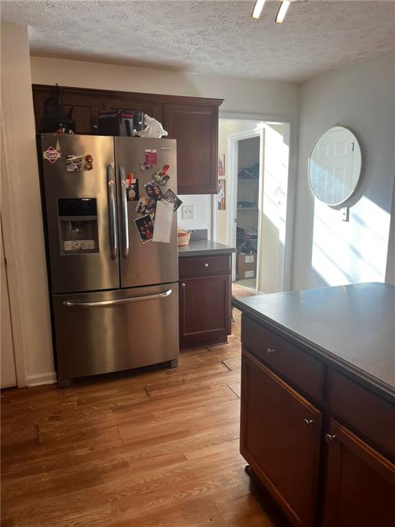 kitchen featuring dark brown cabinets, stainless steel refrigerator with ice dispenser, light hardwood / wood-style floors, and a textured ceiling