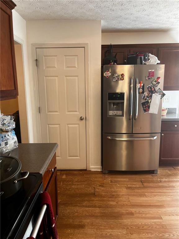 kitchen featuring light hardwood / wood-style flooring, black / electric stove, a textured ceiling, and stainless steel fridge