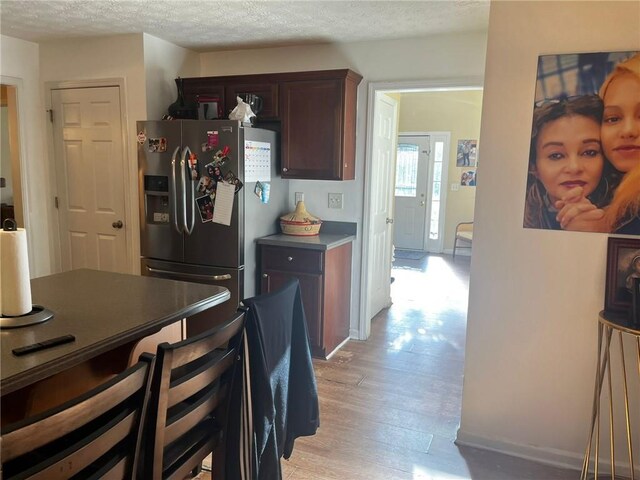 kitchen featuring dark brown cabinets, light hardwood / wood-style flooring, a textured ceiling, and stainless steel fridge with ice dispenser