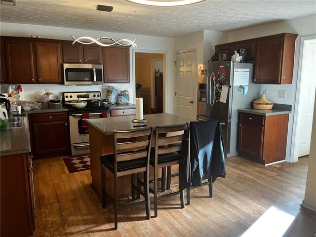 kitchen with appliances with stainless steel finishes, a textured ceiling, decorative light fixtures, light hardwood / wood-style flooring, and a center island