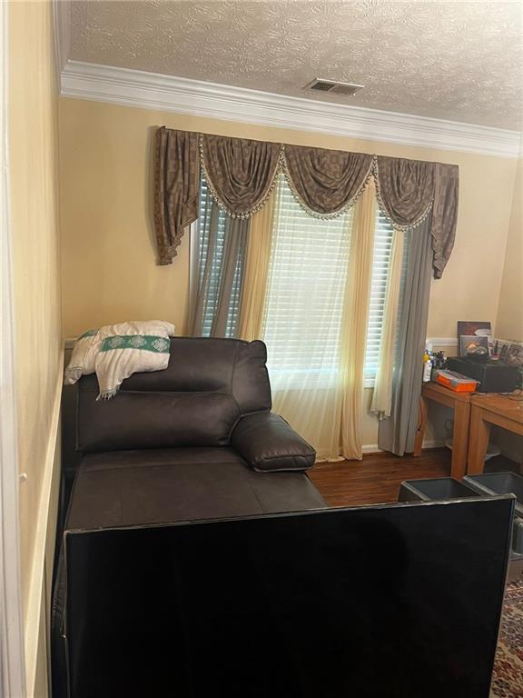 living area featuring wood-type flooring, a textured ceiling, and crown molding