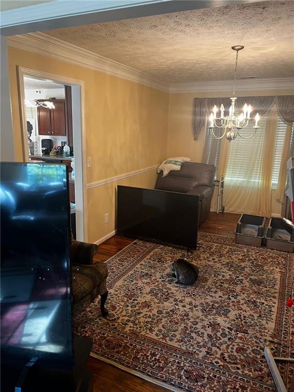 living room with dark hardwood / wood-style flooring, a textured ceiling, an inviting chandelier, and crown molding