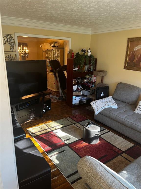 living room with a chandelier, a textured ceiling, dark hardwood / wood-style flooring, and ornamental molding