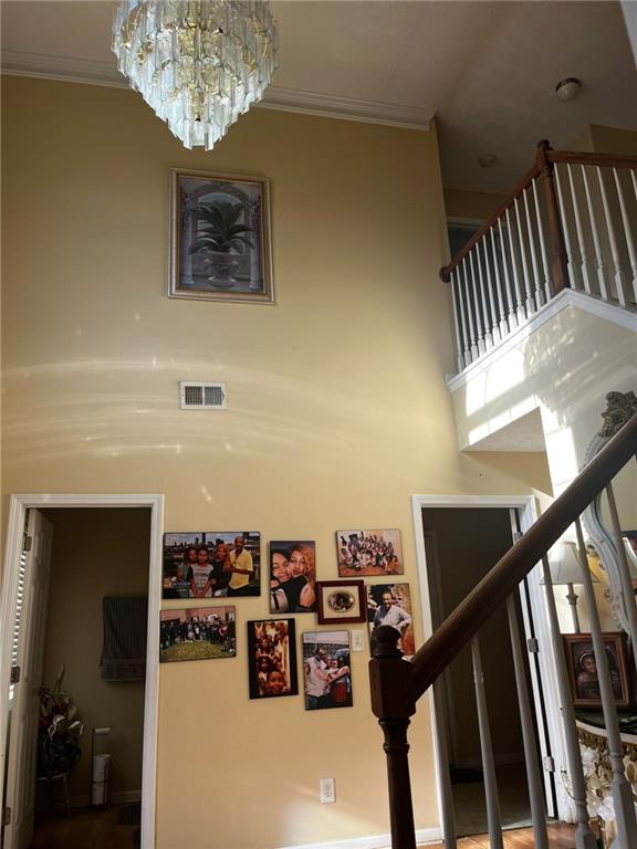 stairs with a high ceiling, a chandelier, and crown molding