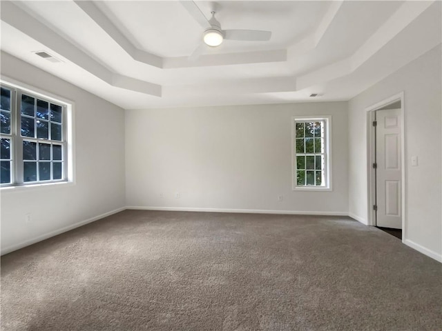 empty room featuring a raised ceiling, carpet flooring, and ceiling fan