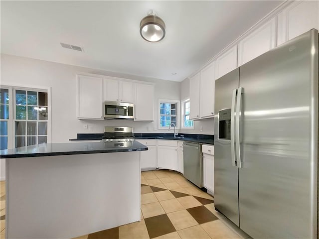 kitchen featuring white cabinetry, light tile patterned floors, stainless steel appliances, a center island, and sink