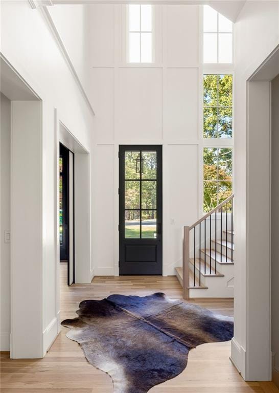 foyer entrance featuring light wood-type flooring, stairs, and a towering ceiling