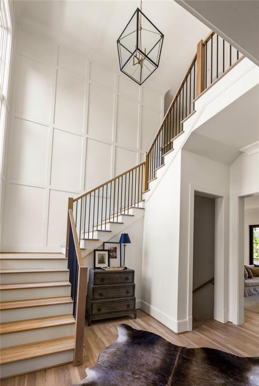 staircase featuring an inviting chandelier, baseboards, a towering ceiling, and wood finished floors