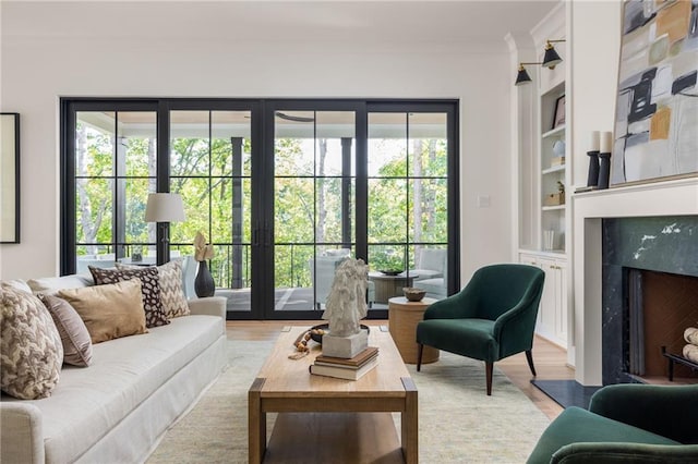 living room with crown molding, a premium fireplace, built in features, and wood finished floors