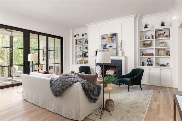 living area with light wood-type flooring, ornamental molding, built in shelves, and a fireplace