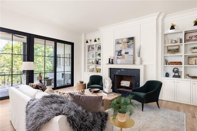 living area with built in shelves, light wood-style floors, crown molding, and a fireplace