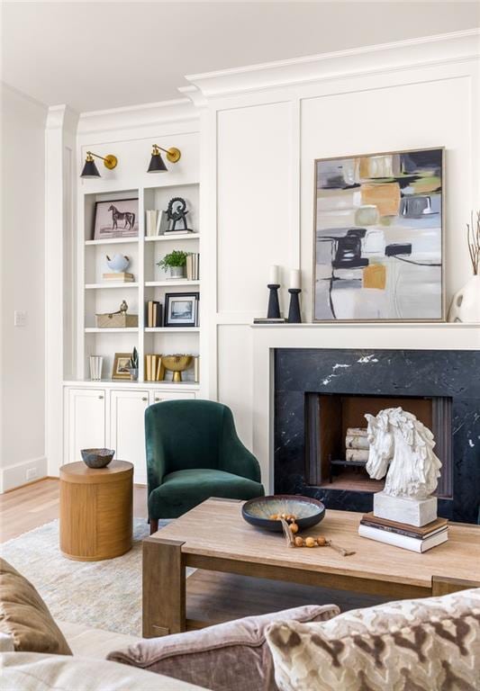 sitting room featuring ornamental molding, a premium fireplace, built in shelves, and wood finished floors