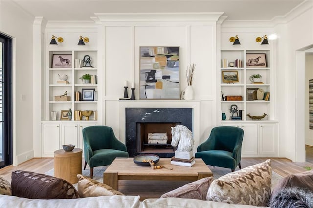 living room featuring ornamental molding, a high end fireplace, built in shelves, and light wood finished floors