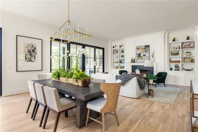 dining area featuring a fireplace, built in features, a chandelier, and light wood finished floors