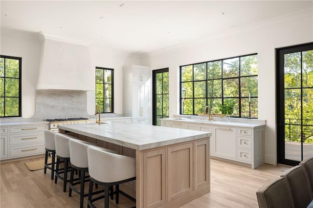 kitchen with tasteful backsplash, light stone counters, light wood finished floors, a center island, and white cabinetry