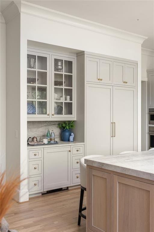 bar with light wood-type flooring, ornamental molding, stainless steel oven, and backsplash