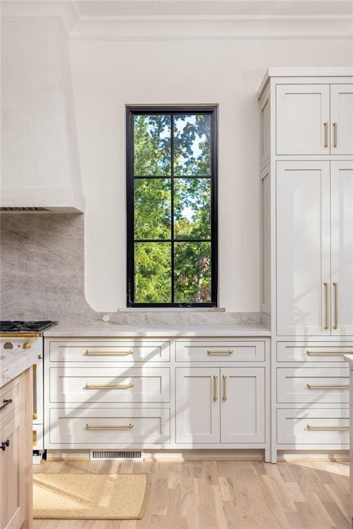 kitchen featuring crown molding, light wood-style floors, backsplash, visible vents, and light stone countertops