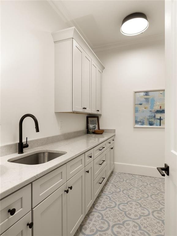 kitchen featuring white cabinets, light stone counters, light tile patterned floors, crown molding, and a sink