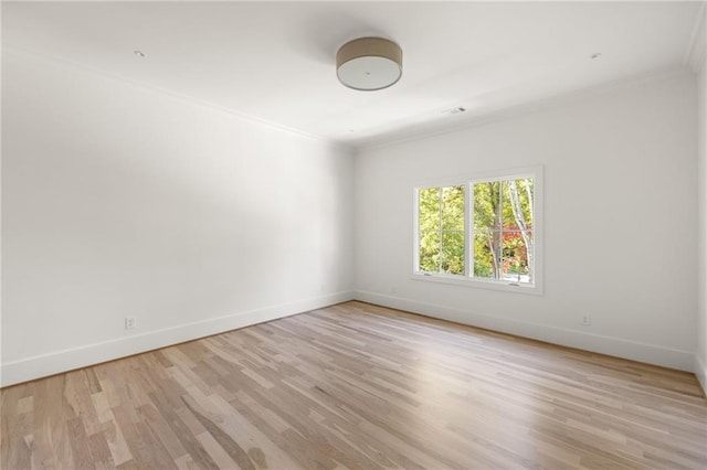 empty room with baseboards, crown molding, and light wood finished floors